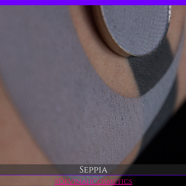 A close-up of a circular makeup eyeshadow matte pigment pan of 'Seppia' eyeshadow with a swatch of the matte eyeshadow. The brand name 'DEVINAH COSMETICS' is visible at the bottom