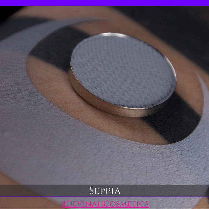 A close-up of a circular makeup eyeshadow matte pigment pan of 'Seppia' eyeshadow with a swatch of the matte eyeshadow. The brand name 'DEVINAH COSMETICS' is visible at the bottom