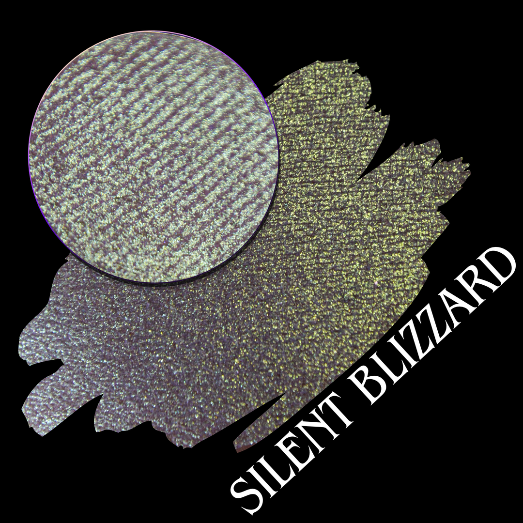 A swatch for 'Silent Blizzard' showing an eyeshadow in a gradient of ice blue to gold on a black background, with a circular makeup eyeshadow pan and the name 'SILENT BLIZZARD' hand made eyeshadow by Devinah Cosmetics.