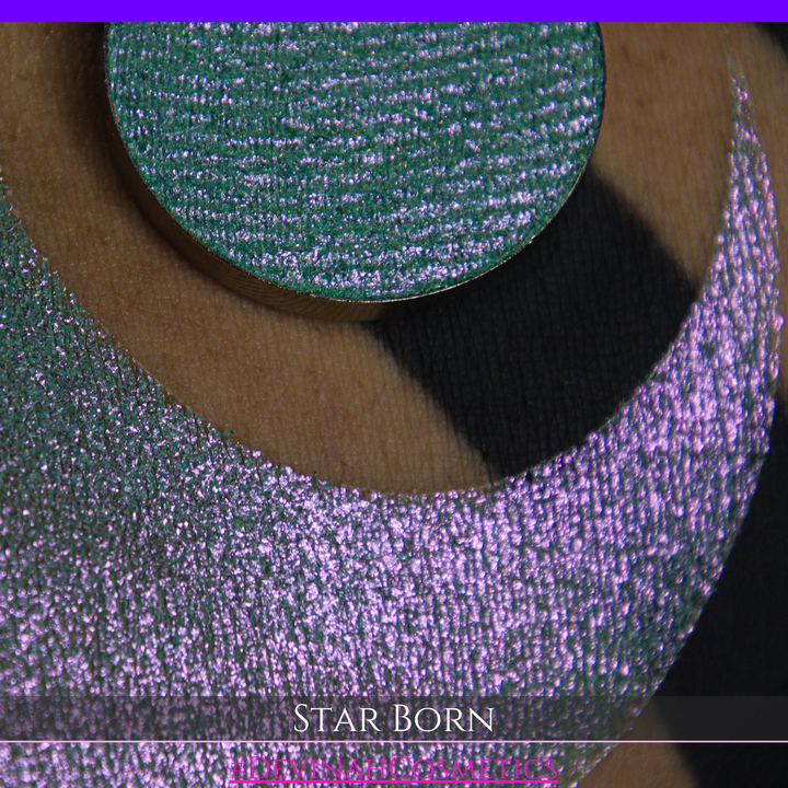 A close-up of a person's skin with a large iridescent crescent moon makeup swatch and a matching circular eyeshadow pan in the center. The text 'STAR BORN' and 'Devinah Cosmetics' appears at the bottom.