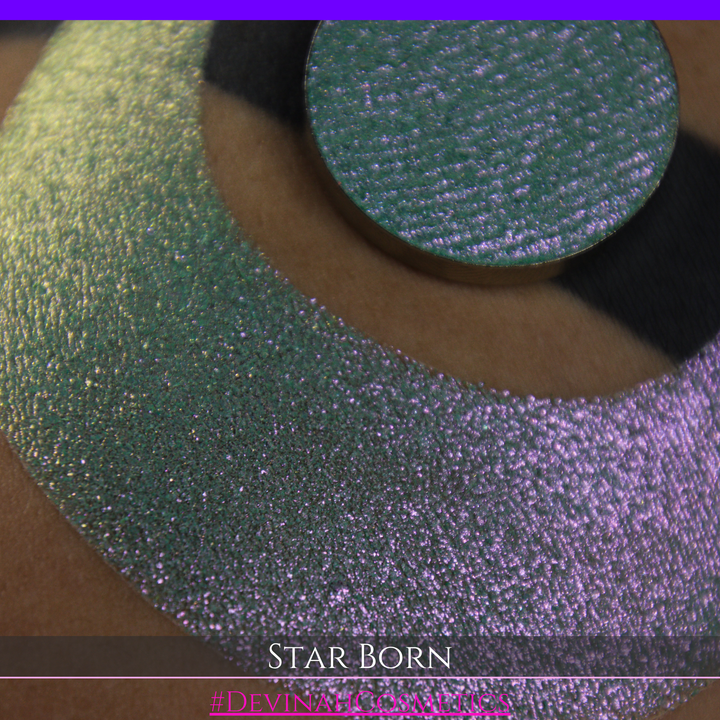A close-up of a person's skin with a large iridescent crescent moon makeup swatch and a matching circular eyeshadow pan in the center. The text 'STAR BORN' and 'Devinah Cosmetics' appears at the bottom.