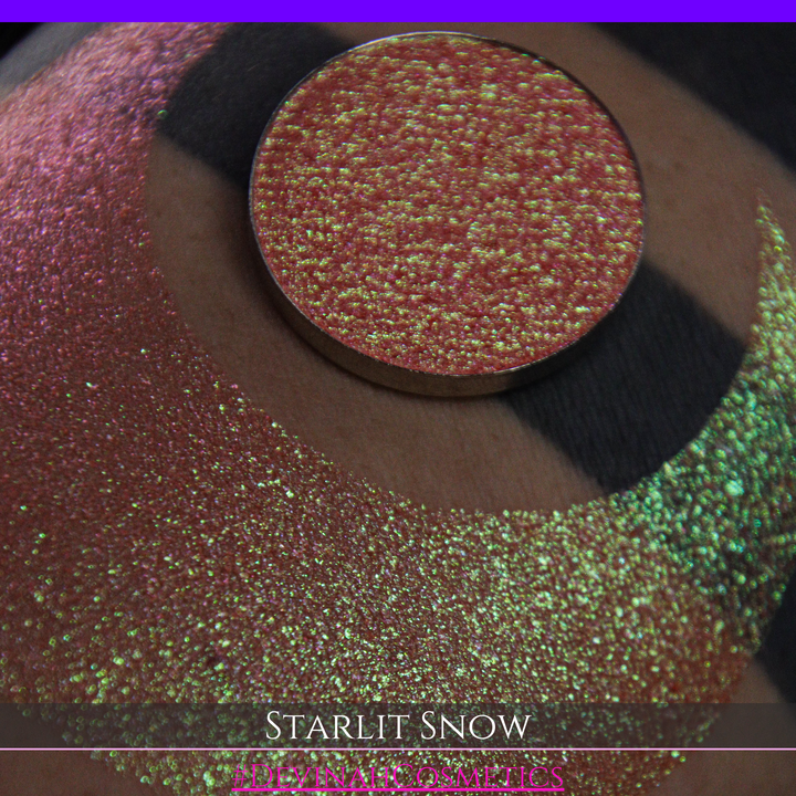 A close-up of a person's arm with a large eyeshadow swatch in a crescent shape and a matching round eyeshadow pan placed in the center. Text at the bottom reads 'STARLIT SNOW' and '#DEVINAHCosmetics'.