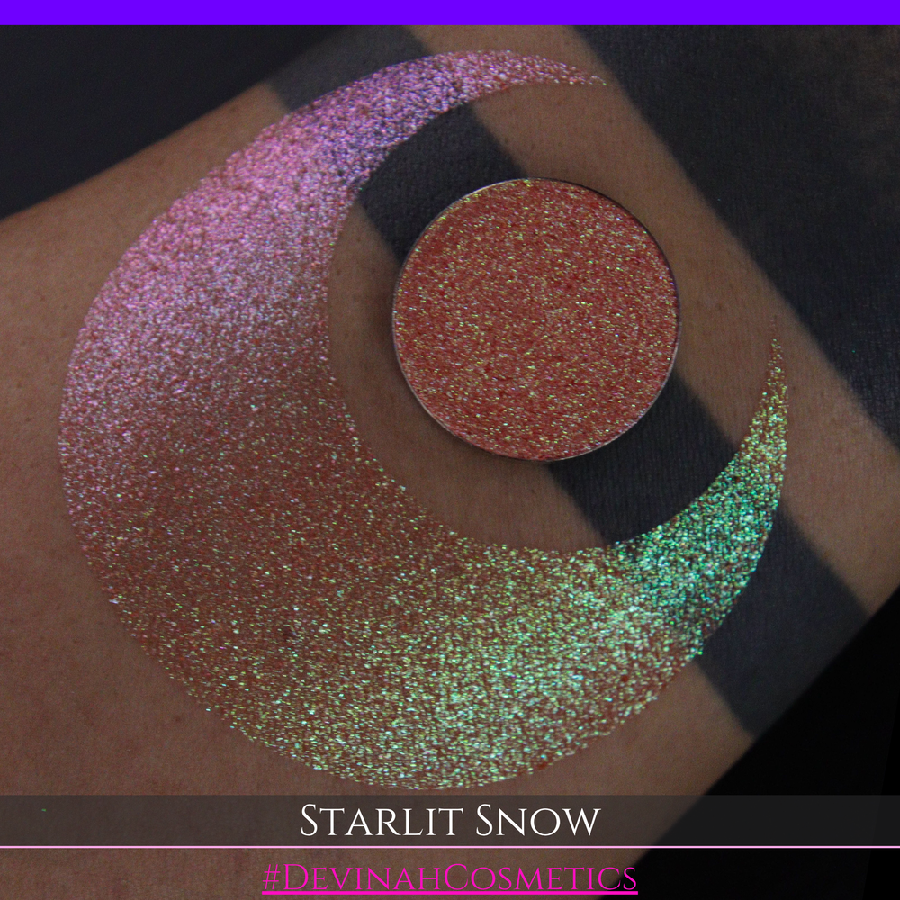 A close-up of a person's arm with a large eyeshadow swatch in a crescent shape and a matching round eyeshadow pan placed in the center. Text at the bottom reads 'STARLIT SNOW' and '#DEVINAHCosmetics'.