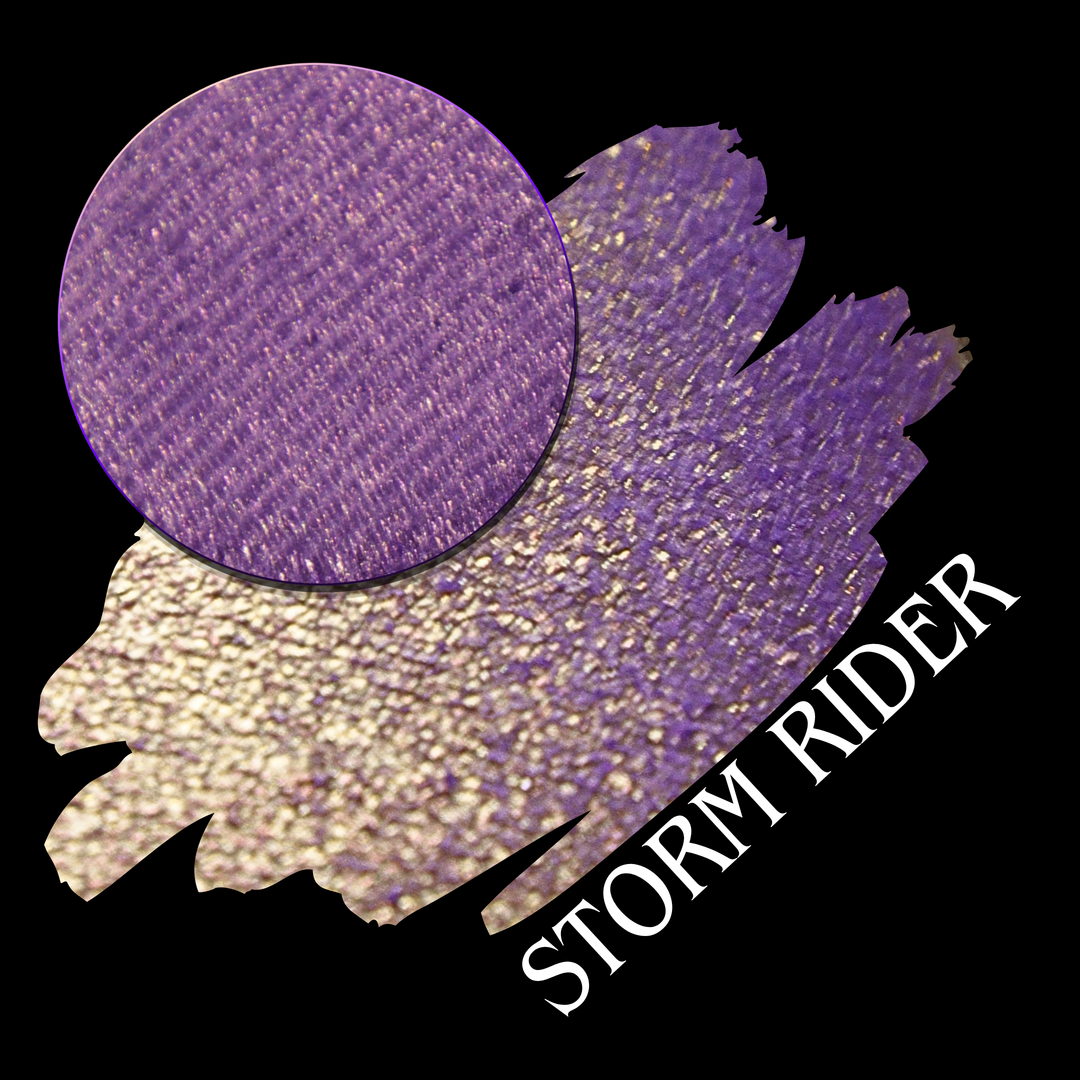 A eyeshadow swatch showing a circular close-up of a purple to golden yellow eyeshadow pan on a black background, with the text 'STORM RIDER' in white made by Devinah Cosmetics.