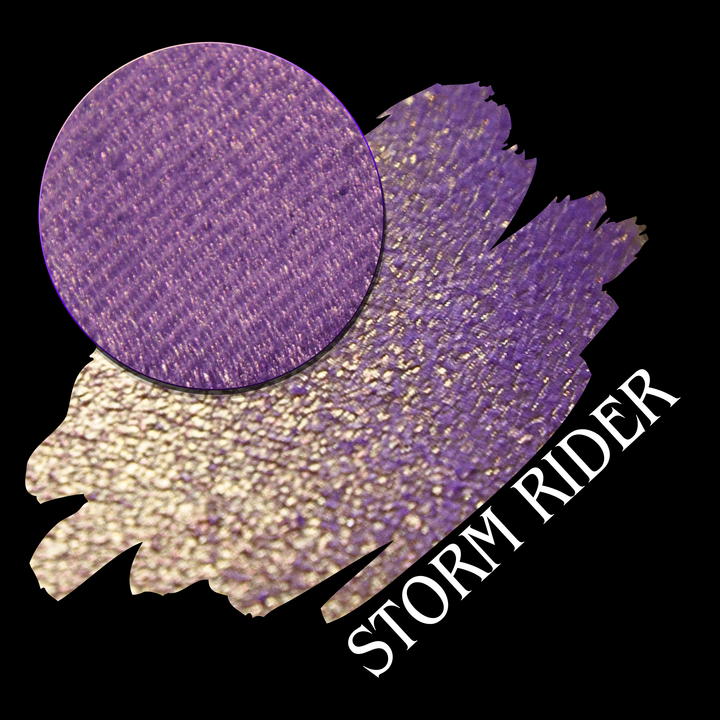 A eyeshadow swatch showing a circular close-up of a purple to golden yellow eyeshadow pan on a black background, with the text 'STORM RIDER' in white made by Devinah Cosmetics.