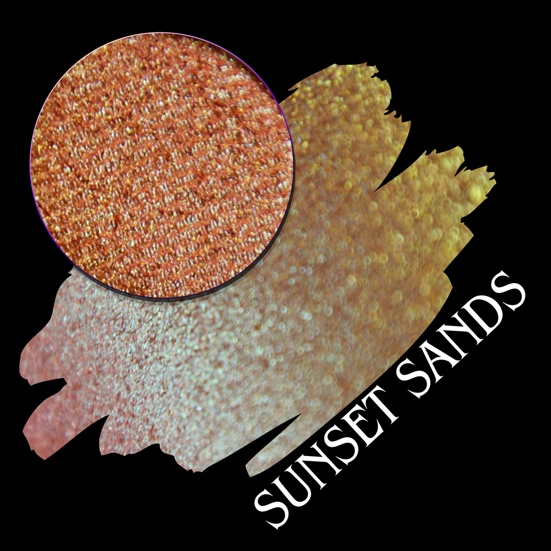 A round eyeshadow pan labeled 'SUNSET SANDS' made by Devinah Cosmetics, placed over a large crescent moon swatch of the same shimmering shifty eyeshadow on skin. The eyeshadow has a duochrome multichrome shift between colors peachy coral pink, orange, yellow, gold.
