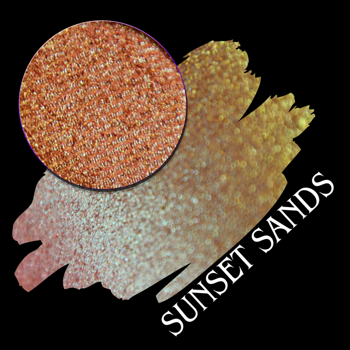 A round eyeshadow pan labeled 'SUNSET SANDS' made by Devinah Cosmetics, placed over a large crescent moon swatch of the same shimmering shifty eyeshadow on skin. The eyeshadow has a duochrome multichrome shift between colors peachy coral pink, orange, yellow, gold.