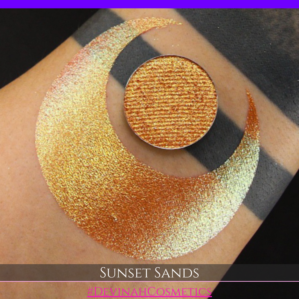 A round eyeshadow pan labeled 'SUNSET SANDS' made by Devinah Cosmetics, placed over a large crescent moon swatch of the same shimmering shifty eyeshadow on skin. The eyeshadow has a duochrome multichrome shift between colors peachy coral pink, orange, yellow, gold.