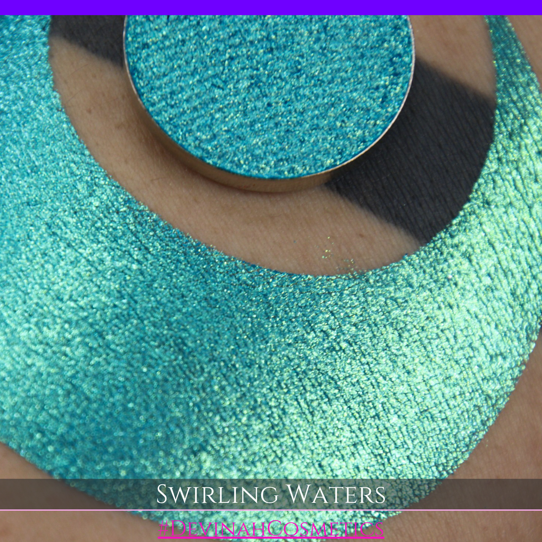 A round eyeshadow pan labeled 'SWIRLING WATERS' made by Devinah Cosmetics, placed over a large crescent moon swatch of the same shimmering shifty eyeshadow on skin. The eyeshadow has a duochrome multichrome shift between colors teal, blue, green.