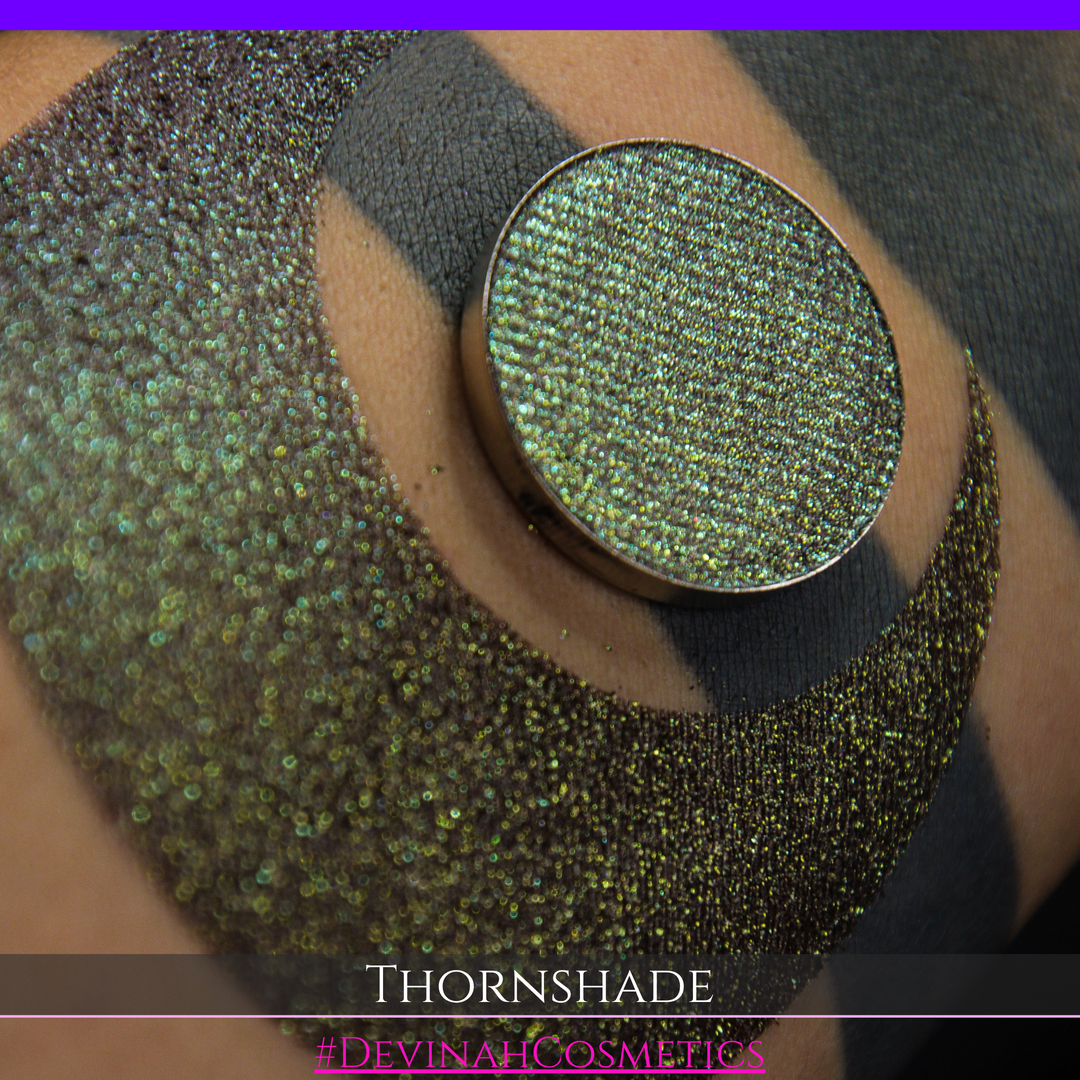 A close-up of a person's arm with a large crescent-shaped swatch of shimmering brown to green eyeshadow, alongside a round eyeshadow pan showing the product texture. Text at the bottom reads 'THORNSHADE' and '#DEVINAHCOSMETICS'.
