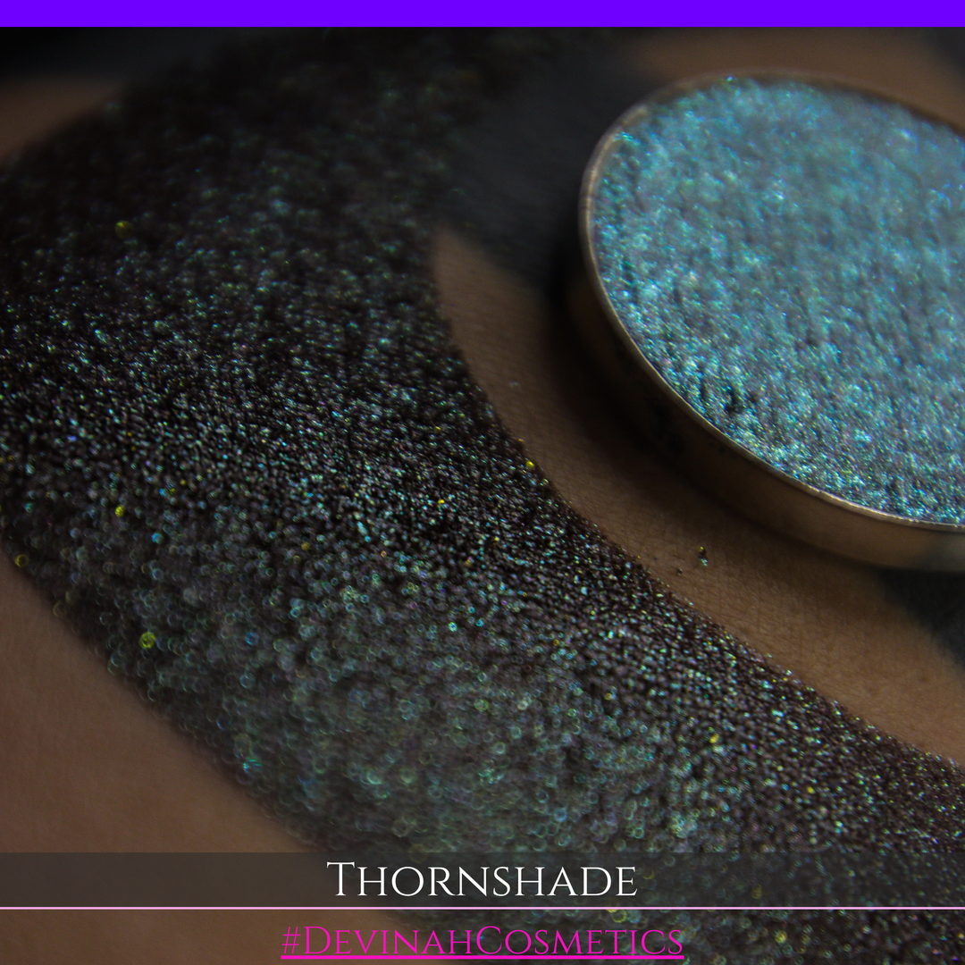 A close-up of a person's arm with a large crescent-shaped swatch of shimmering brown to green eyeshadow, alongside a round eyeshadow pan showing the product texture. Text at the bottom reads 'THORNSHADE' and '#DEVINAHCOSMETICS'.