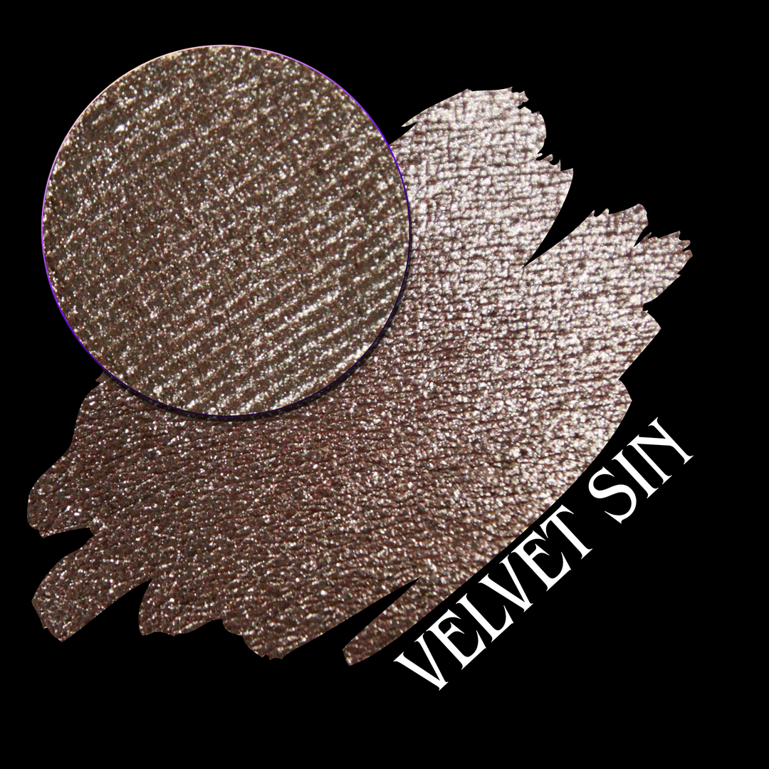 A round eyeshadow pan labeled 'VELVET SIN' made by Devinah Cosmetics, placed over a large crescent moon swatch of the same shimmering shifty eyeshadow on skin. The eyeshadow has colors of beige tan creme colored shimmer.