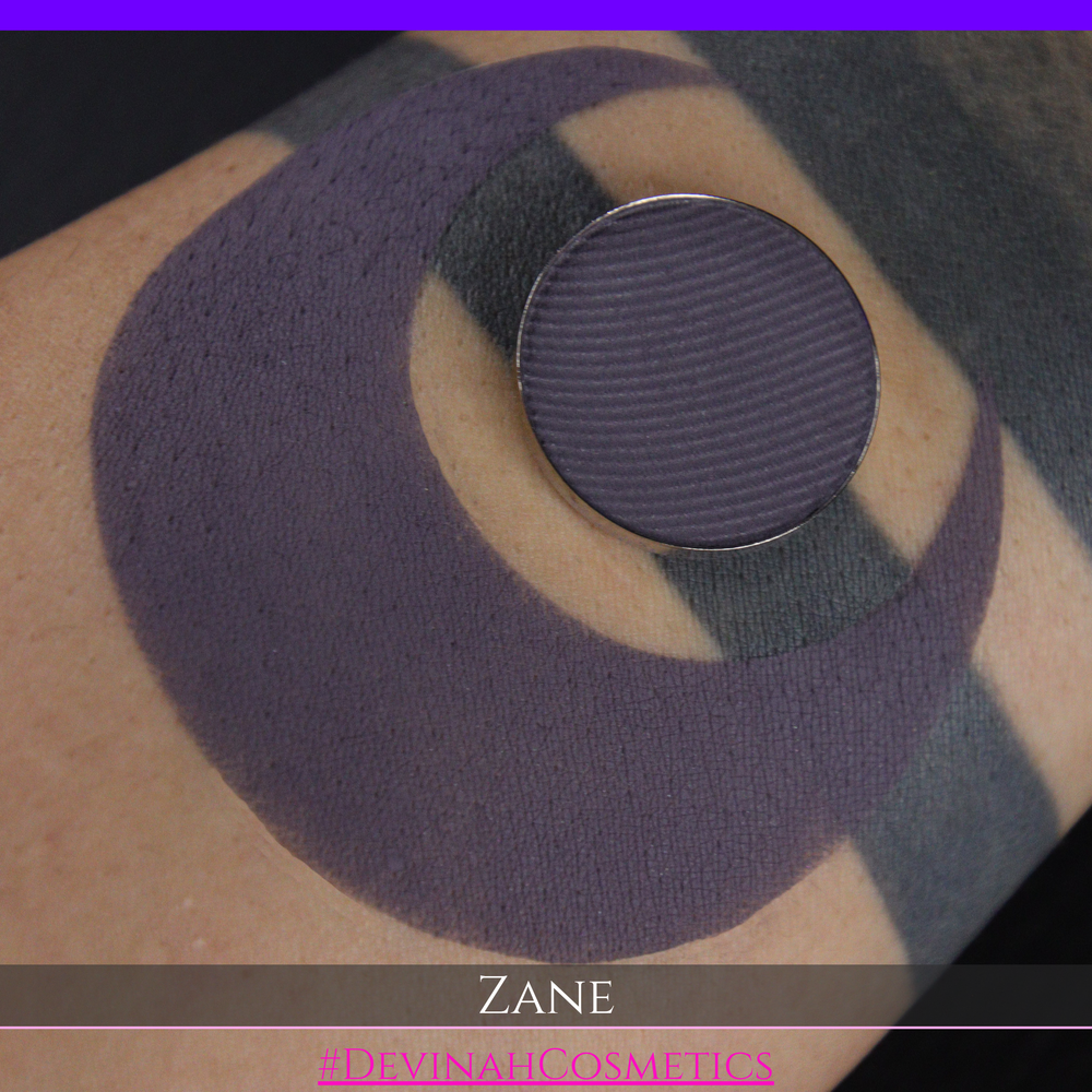 A makeup swatch showing a dark plum-purple eyeshadow color with a circular makeup pan and the name 'ZANE' in white text on a black background.