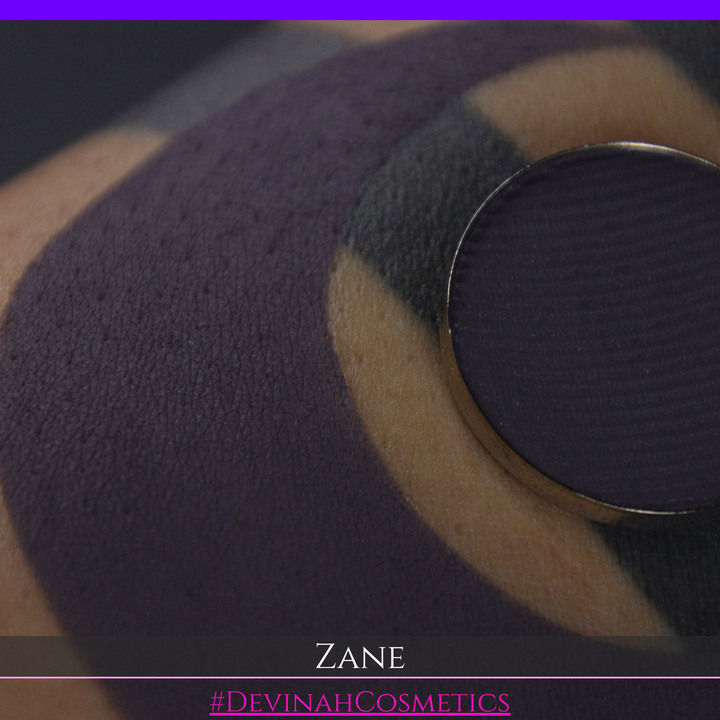 A makeup swatch showing a dark plum-purple eyeshadow color with a circular makeup pan and the name 'ZANE' in white text on a black background.