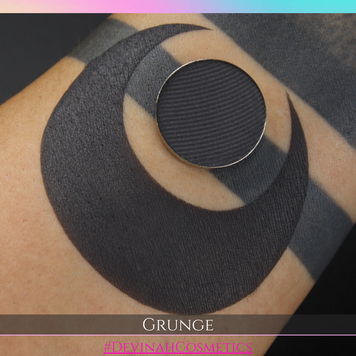 Black circular eyeshadow pan on skin with a swatch of matte eyeshadow pigment and 'Grunge' text and 'Devinah Cosmetics' branding.
