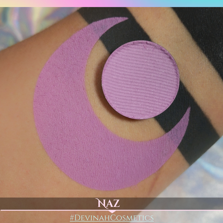 Close-up of a purple circular makeup eyeshadow pan on skin with 'NAZ' and '#DEVINAH COSMETICS' branding.