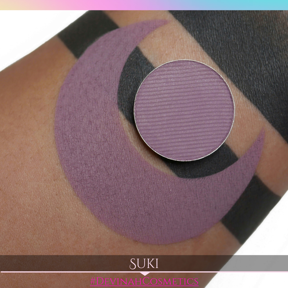Purple makeup shade swatched on skin with 'SUKI' and '#DEVINAH COSMETICS' branding.