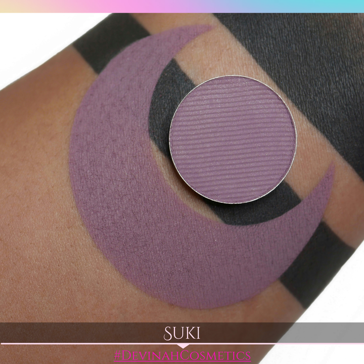 Purple makeup shade swatched on skin with 'SUKI' and '#DEVINAH COSMETICS' branding.